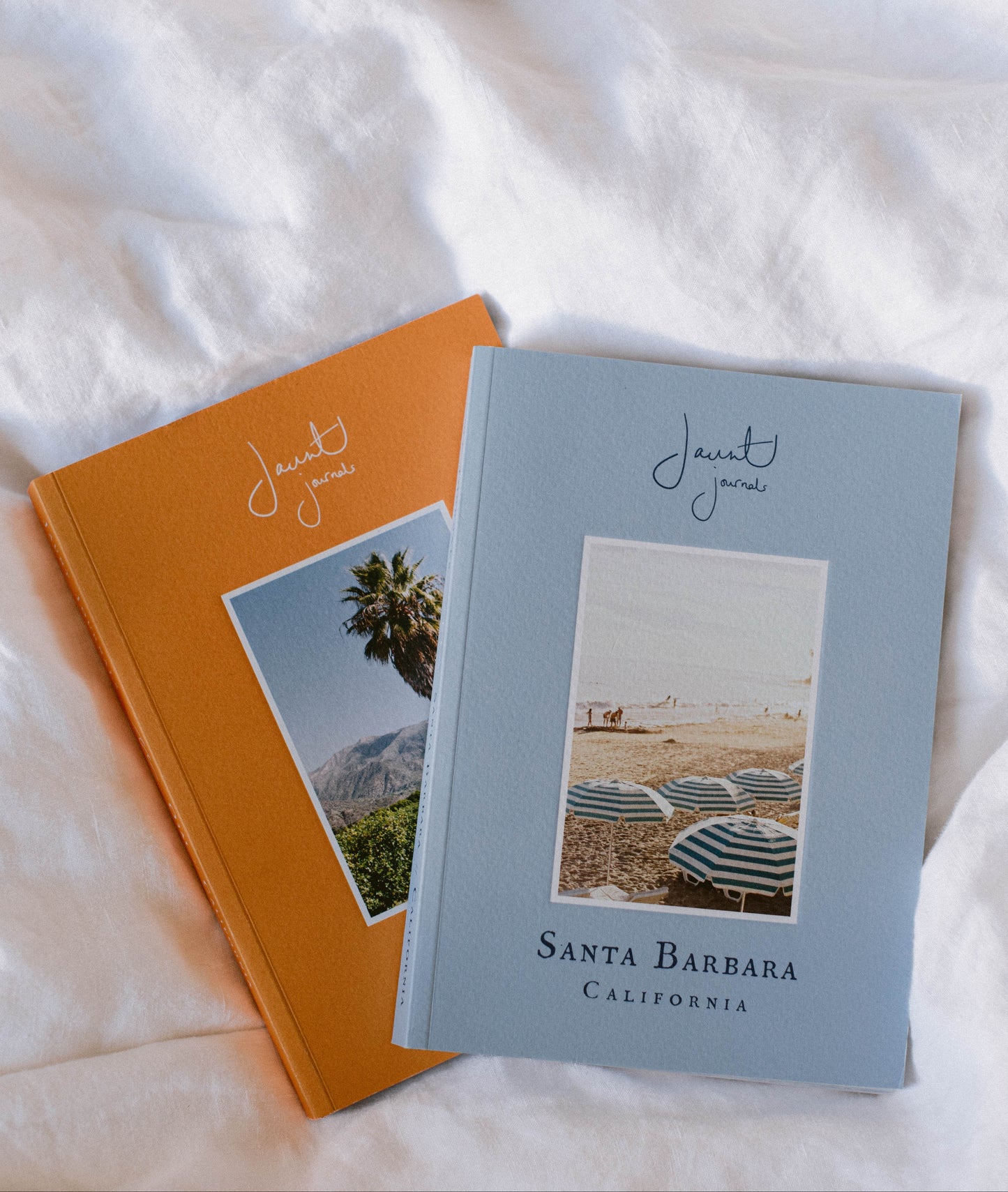 Two books with travel-themed covers on a white fabric background